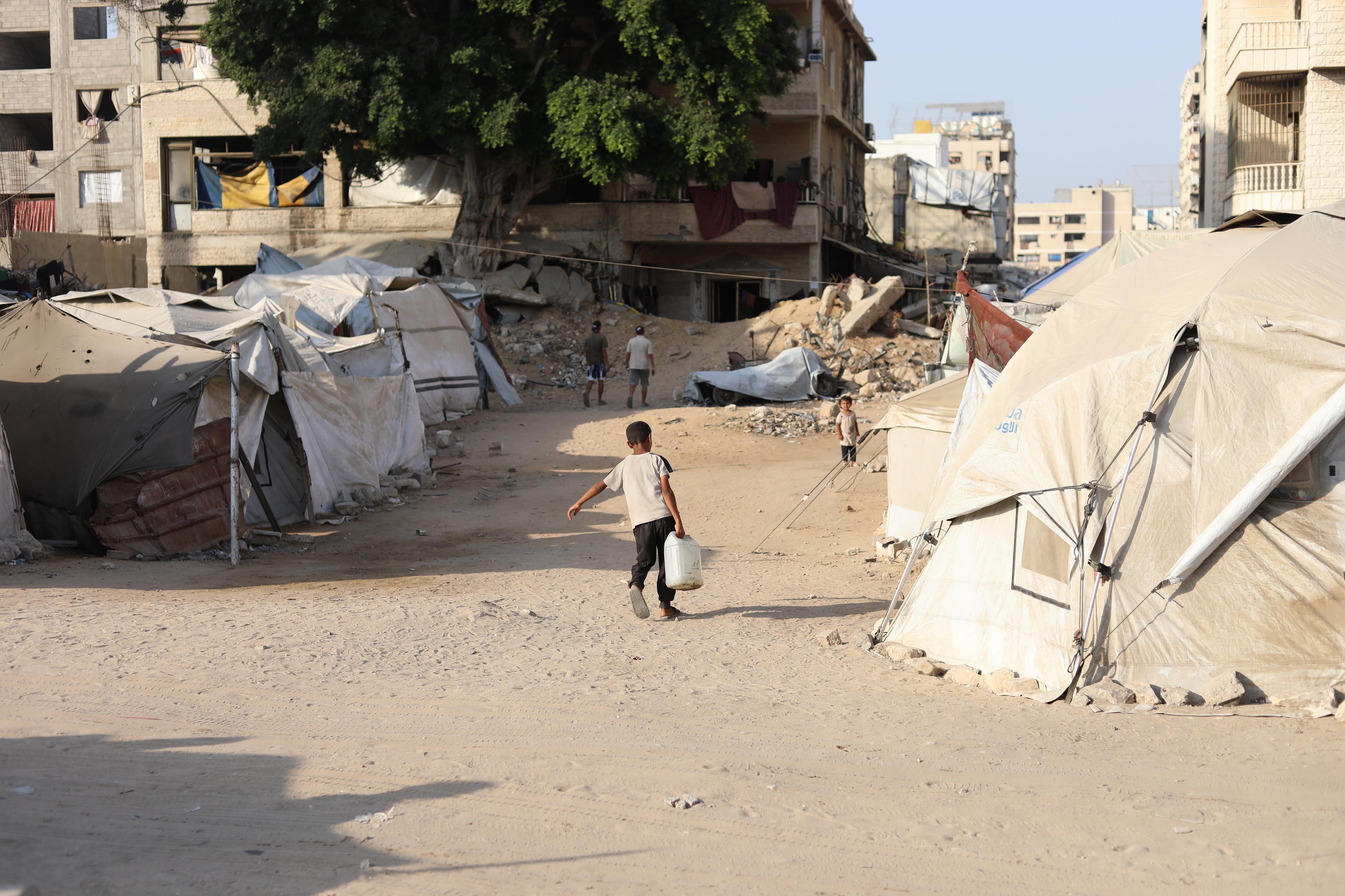 Un petit garçon lutte sous le poids d'un jerrycan d'eau pour le ramener à la tente de sa famille déplacée.